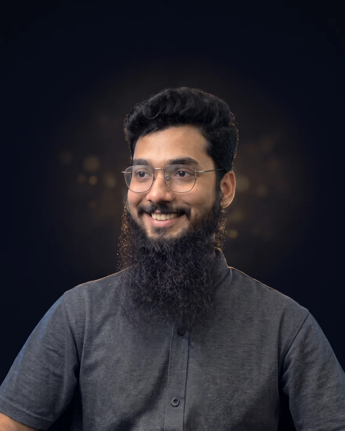 Jawad Nisar, smiling and looking to the side, in a grey shirt against a dark background